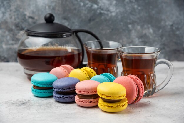 Macarons coloridos con taza de té y dos tazas de té negro sobre superficie blanca.