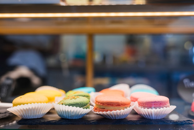 Foto gratuita macarrones de colores en el soporte de papel para cupcakes dentro de la vitrina