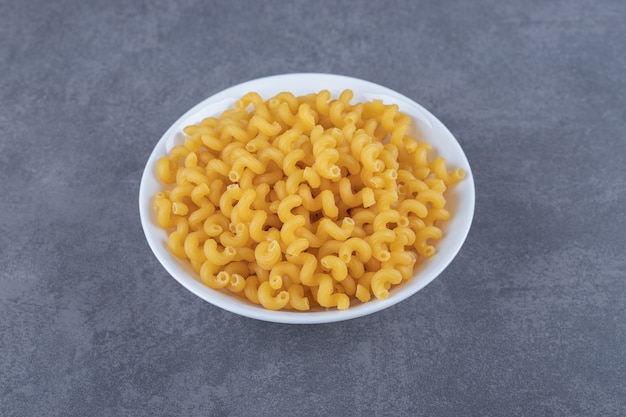 Macarrones crudos del codo en la placa blanca.