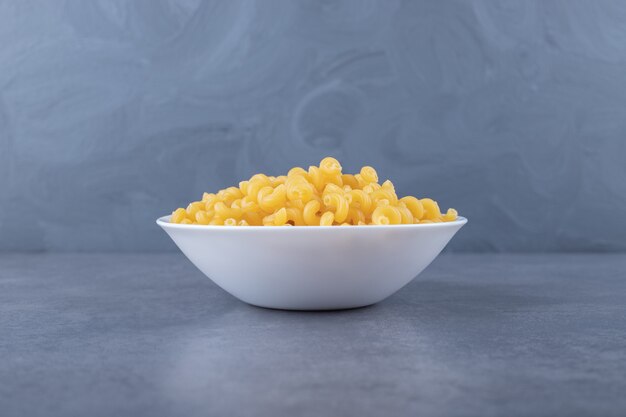 Macarrones crudos del codo en la placa blanca.