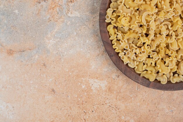 Macarrones crudos frescos sobre tabla de madera en espacio de mármol