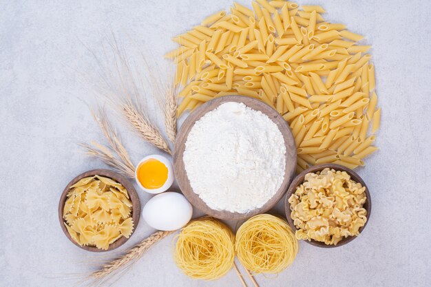 Macarrones crudos en tazón de madera con yema y harina