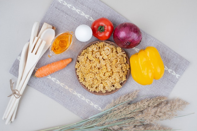 Foto gratuita macarrones crudos con verduras en placa de madera sobre mantel