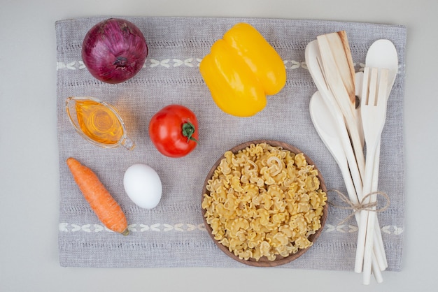 Macarrones crudos con verduras en placa de madera sobre mantel