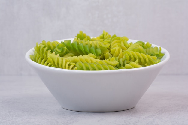 Macarrones en espiral sin cocer verde fresco en la placa blanca.