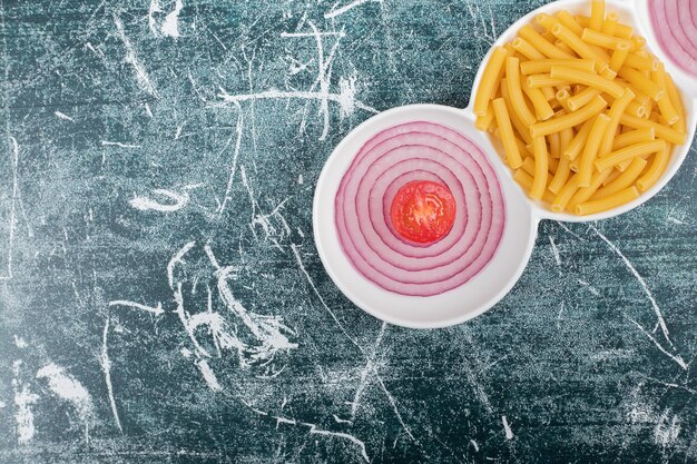 Macarrones frescos sin preparar con rodajas de cebolla y tomate cherry. Foto de alta calidad