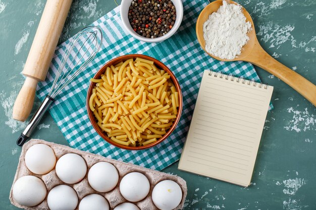 Macarrones con huevos, rodillo, batidor, granos de pimienta, almidón y cuaderno