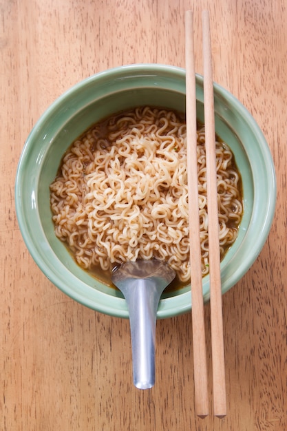 Foto gratuita macarrones instantáneos con cuchara y palillos en un recipiente de cerámica sobre fondo de madera