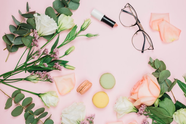 Macarrones; lápiz labial; anteojos con rosa; Flor de limonium y eustoma sobre fondo rosa