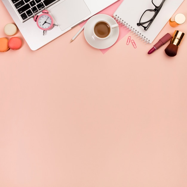 Foto gratuita macarrones, pinceles de maquillaje con reloj despertador en la computadora portátil y papelería sobre fondo de melocotón