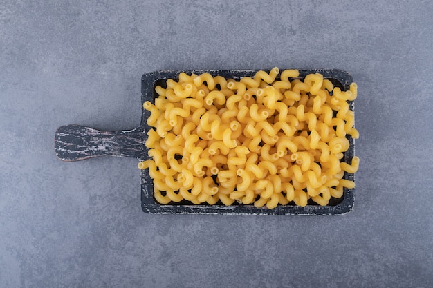 Macarrones secos crudos sobre tabla de madera negra.