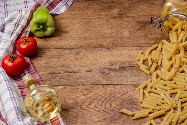 Macarrones, tomates, pimentón y aceite en la mesa de madera listos para cocinar pasta