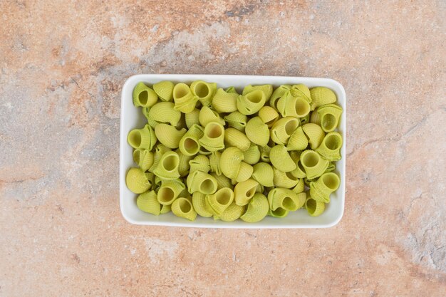 Macarrones verdes sin preparar en plato blanco en espacio de mármol.