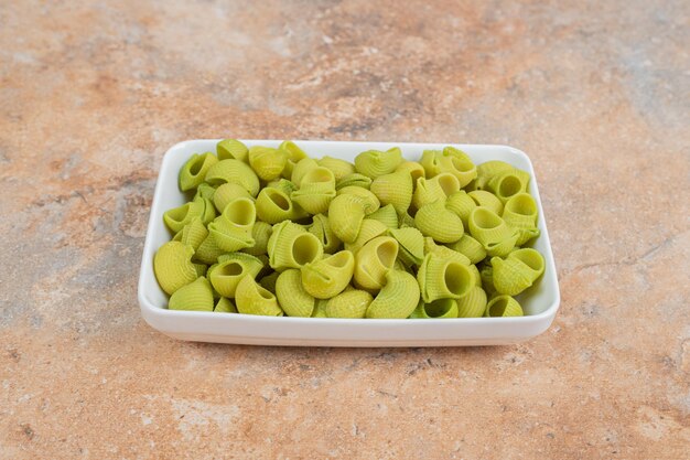 Macarrones verdes sin preparar en plato blanco en espacio de mármol.