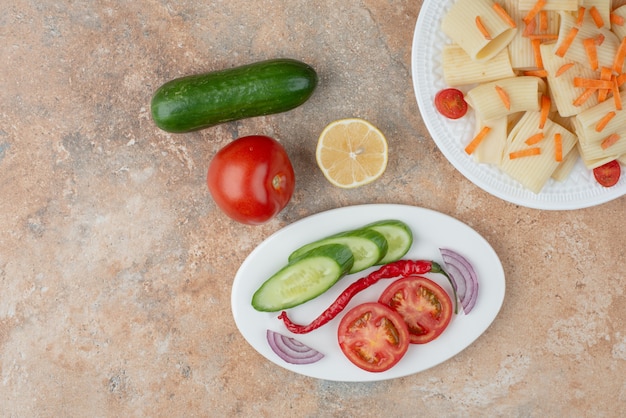 Foto gratuita macarrones con zanahoria, tomate cherry, pepino y rodaja de limón en la placa blanca.