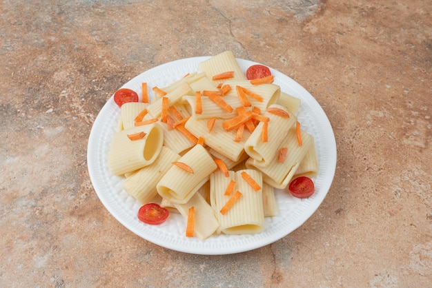 Macarrones con zanahoria y tomate cherry en plato blanco.