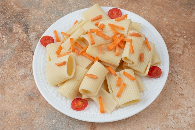 Macarrones con zanahoria y tomate cherry en plato blanco.