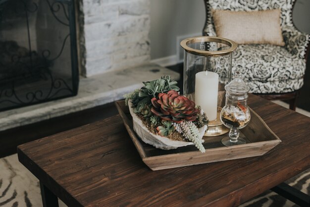 Maceta de madera sobre una mesa de madera con flores y velas cerca de un sillón y una chimenea.