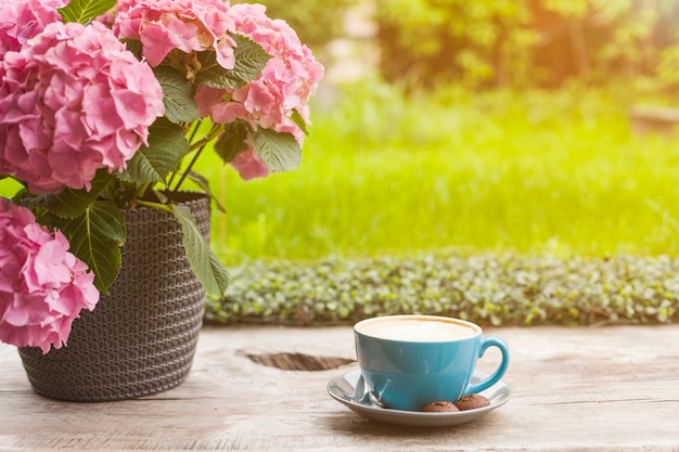 Maceta rosada hermosa y taza de café en superficie de madera