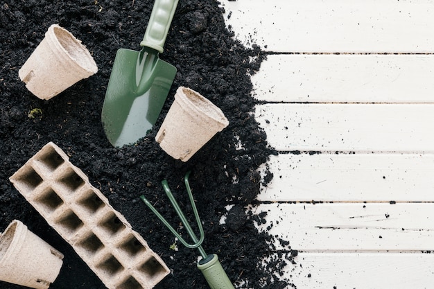 Maceta de turba y bandeja de turba; suelo negro con pala de jardineria; rastrillo de jardinería sobre escritorio de madera