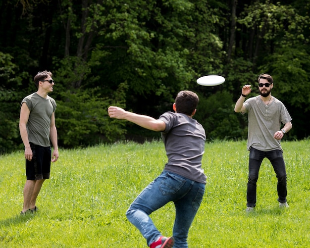 Foto gratuita macho adulto lanzando frisbee para un amigo en el parque