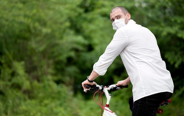 Macho adulto montando bicicleta con mascarilla