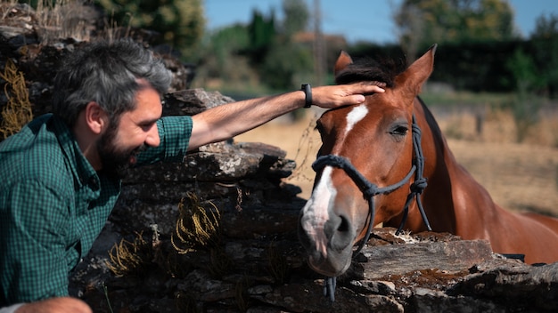 Macho atractivo de mediana edad acariciando la cabeza de un caballo en un rancho