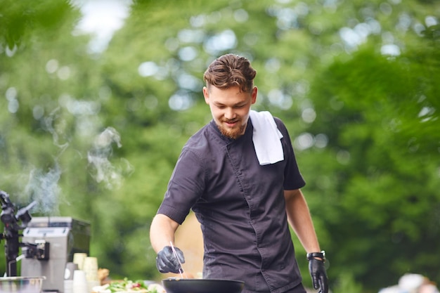 Macho chef sonriente cocinando con pan al aire libre