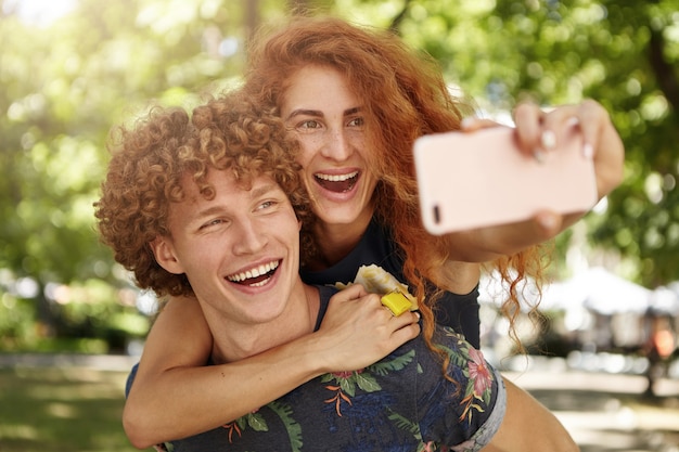 Macho y hembra alegre descansando al aire libre tomando selfies