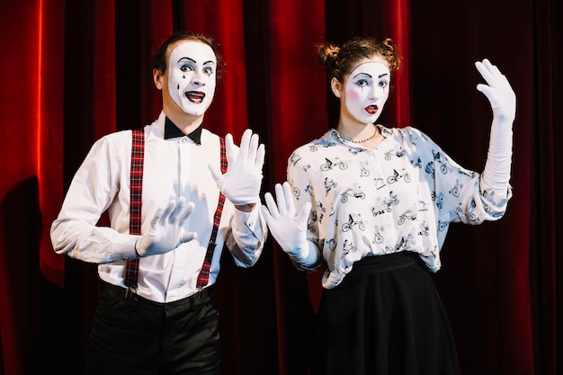 Macho y hembra mime artista de pie delante de la cortina roja que muestra gesto de la mano