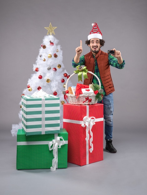 macho joven alrededor de regalos de navidad en gris