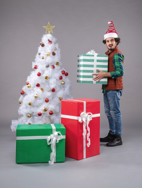 macho joven alrededor de regalos de navidad en gris