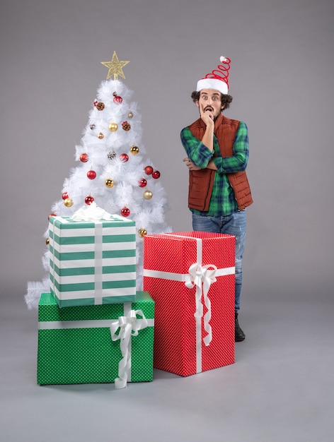 macho joven alrededor de regalos de vacaciones en gris