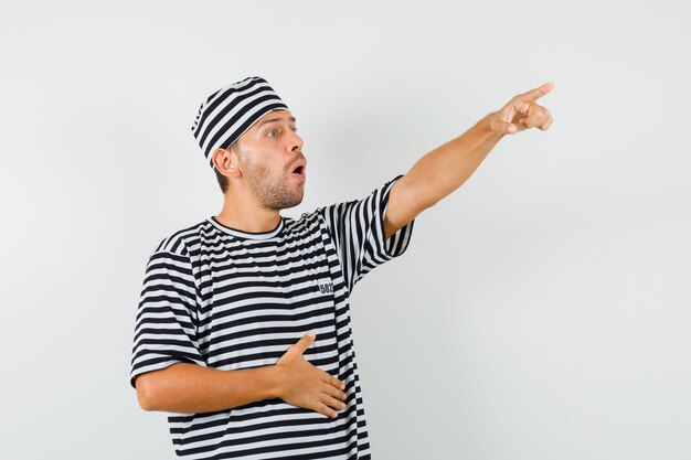 Macho joven apuntando hacia afuera con sombrero de camiseta a rayas y mirando enfocado