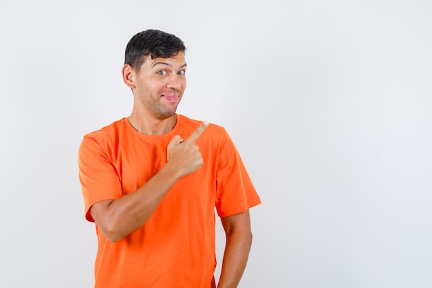Macho joven apuntando el dedo hacia arriba en camiseta naranja y mirando astuto