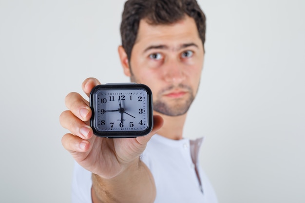 Macho joven apuntando el reloj a la cámara en camiseta blanca