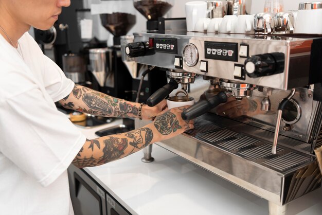 Macho joven barista con tatuajes con la máquina de café en el trabajo