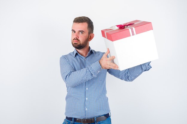 Macho joven con caja de regalo en camisa y mirando enfocado, vista frontal.