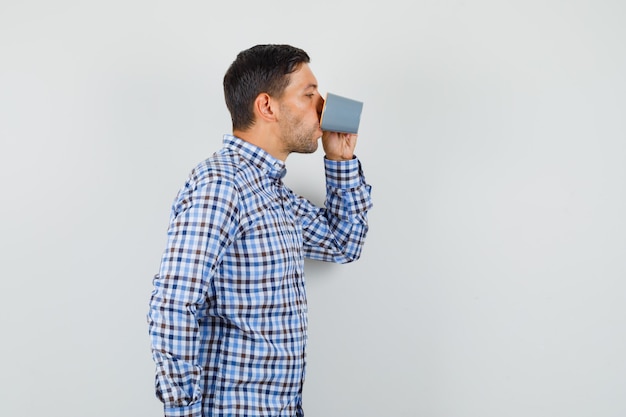 Macho joven en camisa de cuadros bebiendo café