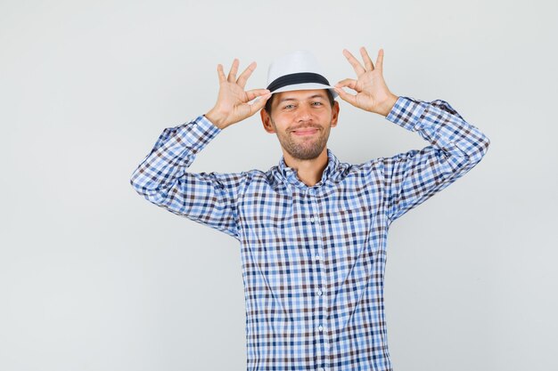 Macho joven en camisa a cuadros sosteniendo su sombrero y mirando feliz