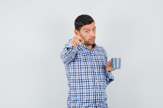 Macho joven en camisa a cuadros sosteniendo una taza de bebida