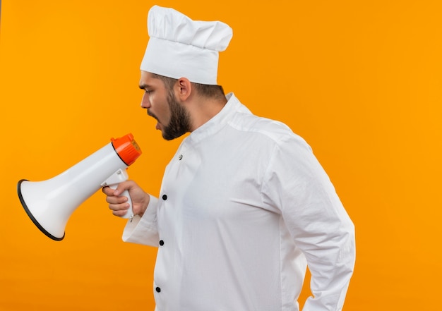 Macho joven cocinero en uniforme de chef hablando por altavoz