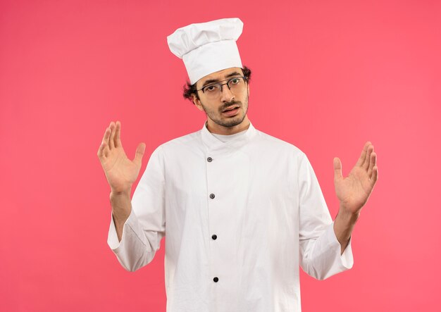 Macho joven cocinero vistiendo uniforme de chef y gafas mostrando el tamaño