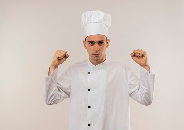 Macho joven cocinero vistiendo uniforme de chef haciendo un gesto fuerte en la pared blanca aislada