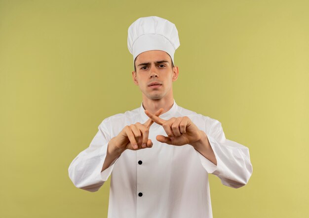 Macho joven cocinero vistiendo uniforme de chef mostrando gesto no en pared verde aislada
