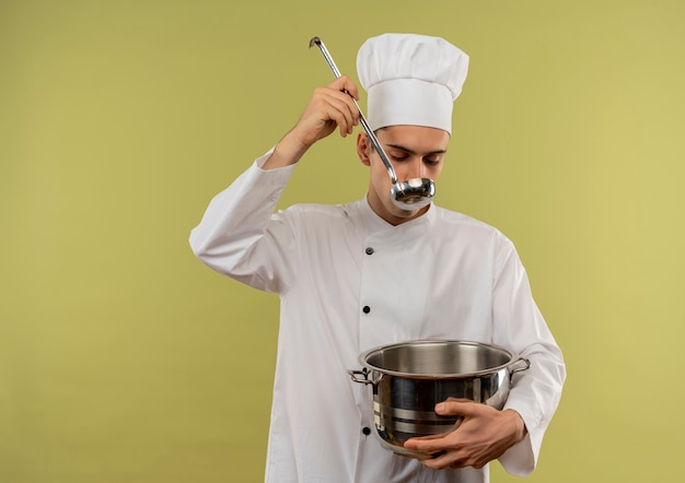 Macho joven cocinero vistiendo uniforme de chef sosteniendo una cacerola tratando de sopa con espacio de copia