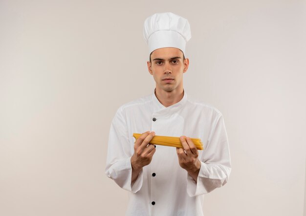 Macho joven cocinero vistiendo uniforme de chef sosteniendo espaguetis en pared blanca aislada con espacio de copia