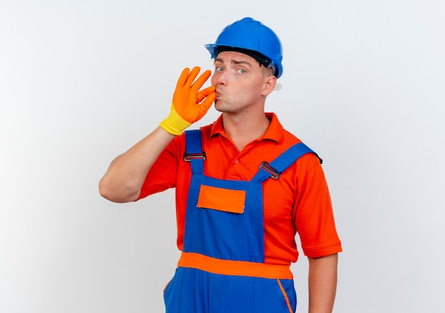 Macho joven constructor vistiendo uniforme y casco de seguridad en guantes mostrando delicioso gesto