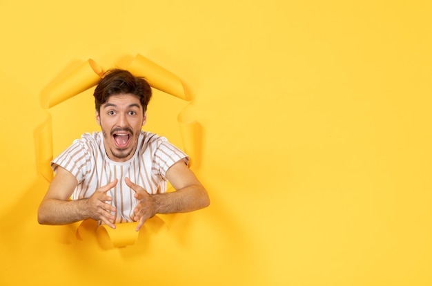 Foto gratuita macho joven emocionado de pie sobre la superficie de papel amarillo rasgado