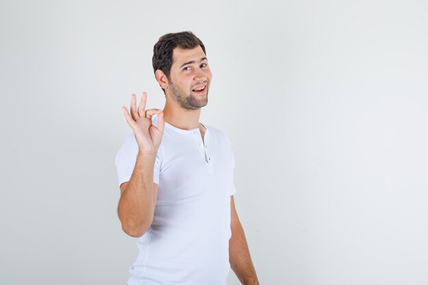 Macho joven haciendo bien firmar y sonriendo en camiseta blanca